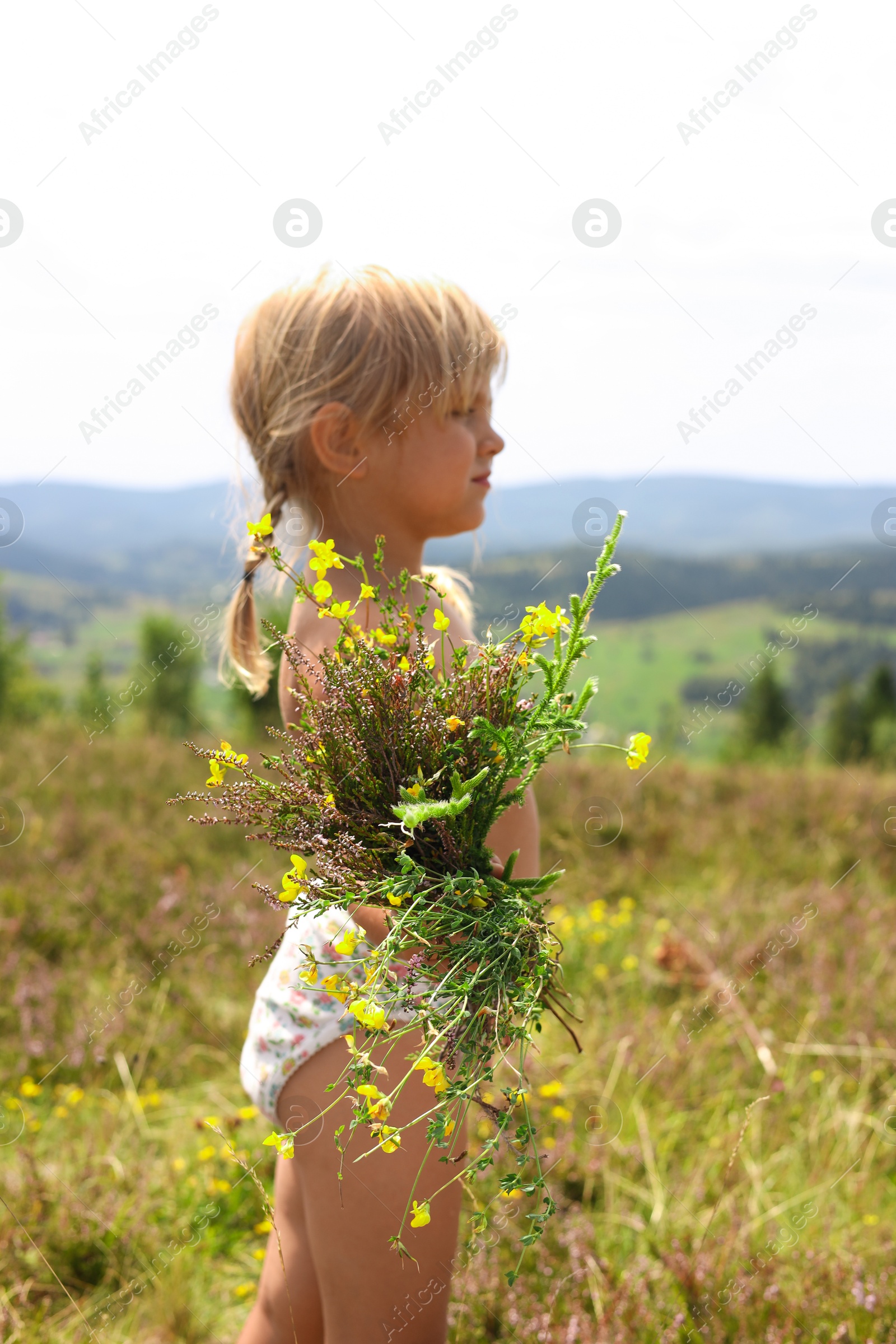 Photo of Smiling little girl with bouquet of wildflowers at field