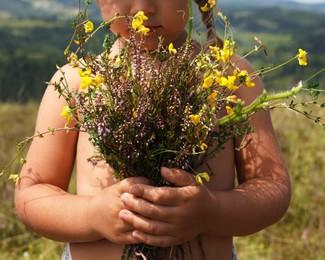 Photo of Little girl with bouquet of wild flowers at field, closeup