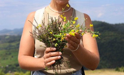 Photo of Woman holding bouquet of wild yellow flowers outdoors, closeup