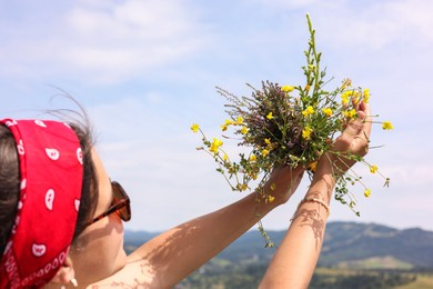 Woman holding bouquet of wild yellow flowers outdoors