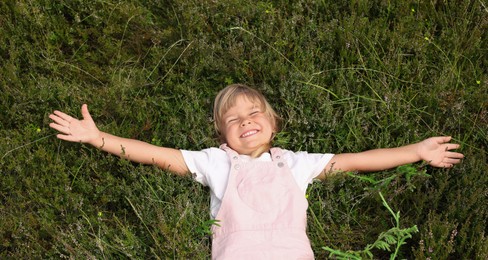 Smiling little girl lying on green grass outdoors, top view