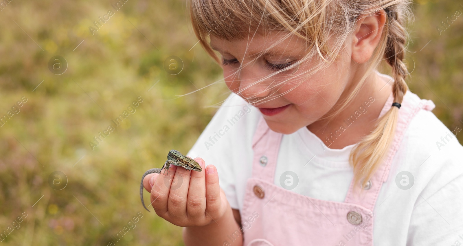 Photo of Happy little girl holding small lizard outdoors, space for text