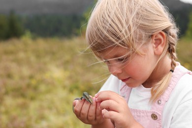 Happy little girl holding small lizard outdoors, space for text