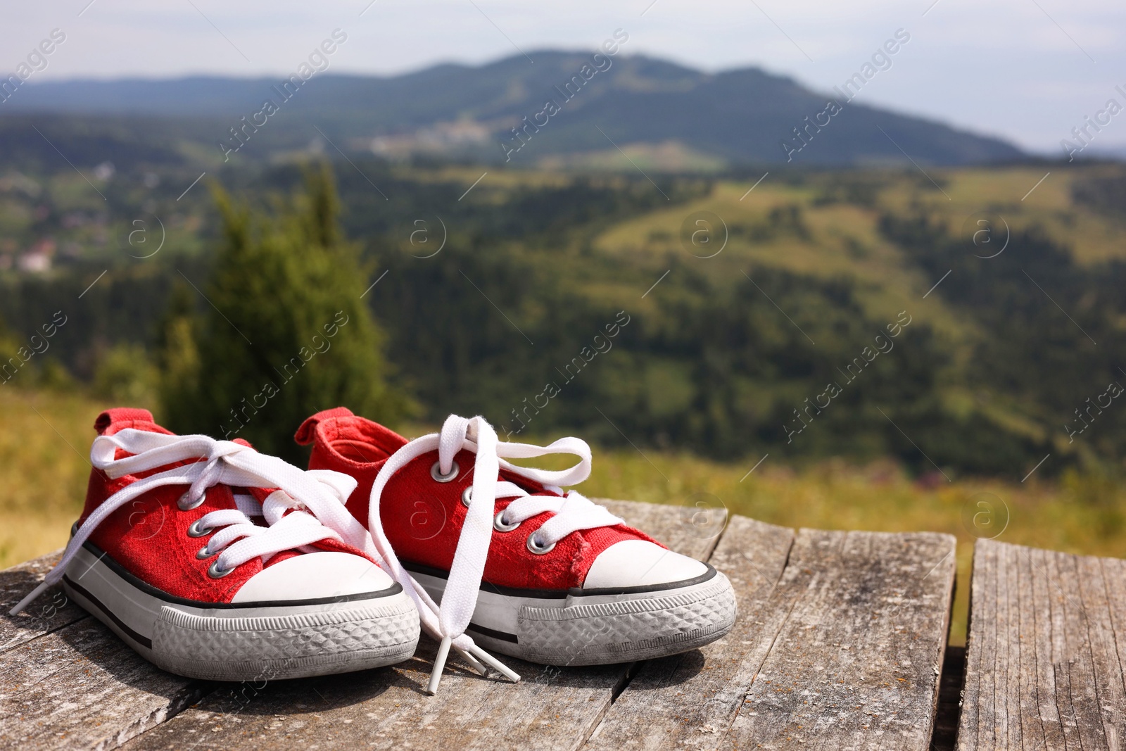 Photo of Pair of red shoes on wooden surface in mountains, space for text