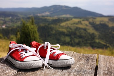 Pair of red shoes on wooden surface in mountains, space for text