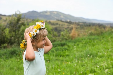 Photo of Smiling little girl in floral wreath at meadow, space for text