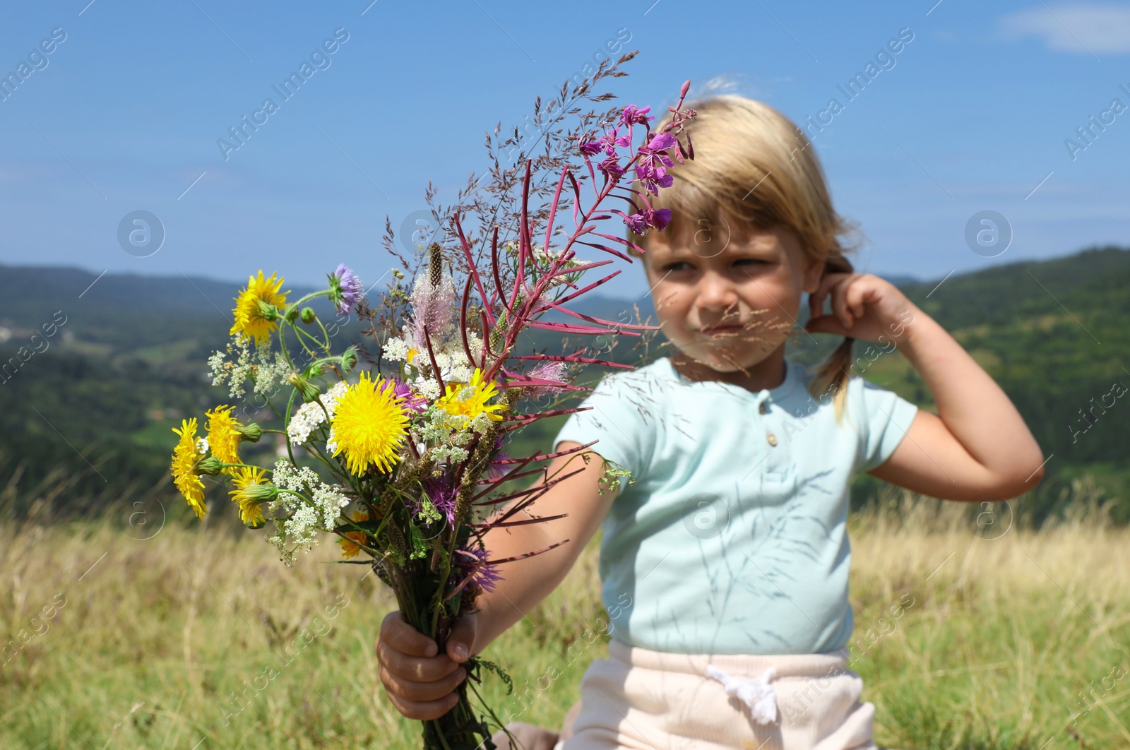 Photo of Smiling little girl with bouquet of wildflowers at field