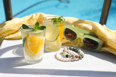 Photo of Tasty cocktail in glasses and sunglasses near swimming pool outdoors