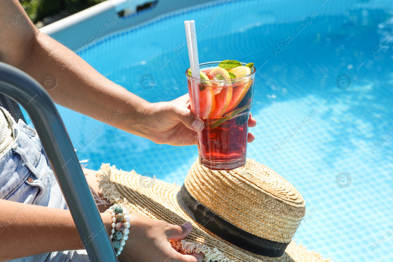 Photo of Woman holding tasty cocktail in glass near swimming pool outdoors, closeup