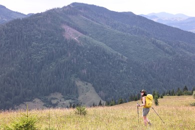 Young hiker with backpack and trekking poles in mountains, space for text