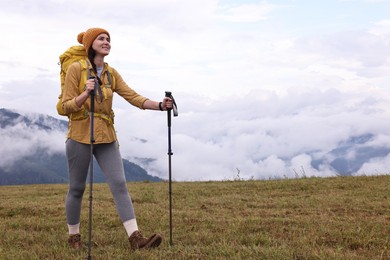 Young hiker with trekking poles and backpack in mountains outdoors, space for text