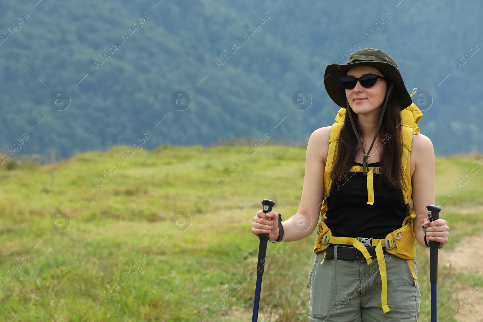 Photo of Young hiker with backpack and trekking poles in mountains, space for text