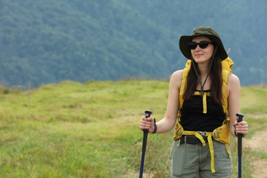 Young hiker with backpack and trekking poles in mountains, space for text