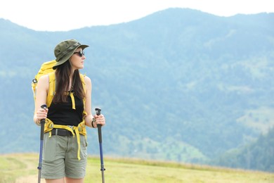 Young hiker with backpack and trekking poles in mountains, space for text