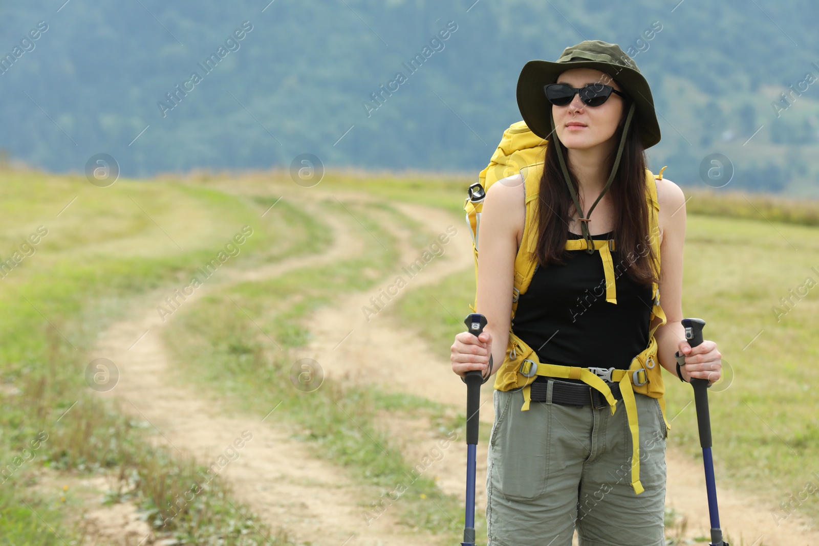 Photo of Young hiker with backpack and trekking poles in mountains, space for text