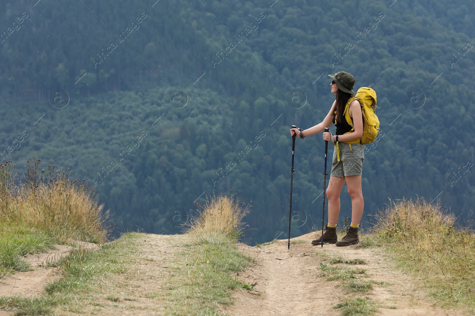 Photo of Young hiker with backpack and trekking poles in mountains, space for text