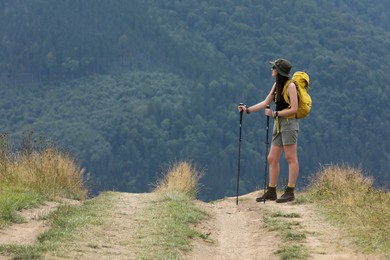 Photo of Young hiker with backpack and trekking poles in mountains, space for text