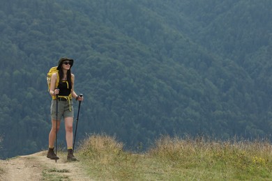 Photo of Young hiker with backpack and trekking poles in mountains, space for text