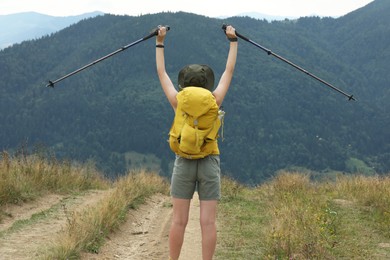 Photo of Young hiker with backpack and trekking poles in mountains, back view