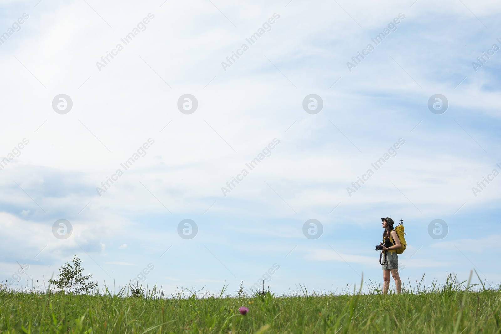 Photo of Young hiker with backpack and camera in field, space for text