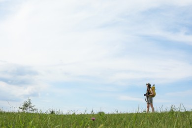 Young hiker with backpack and camera in field, space for text