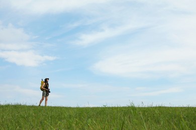 Young hiker with backpack and camera in field, space for text