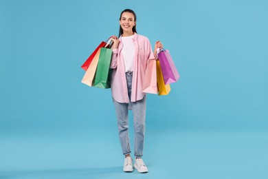 Smiling woman with colorful shopping bags on light blue background