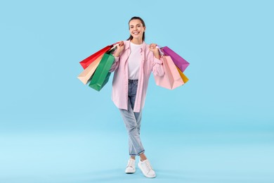 Smiling woman with colorful shopping bags on light blue background