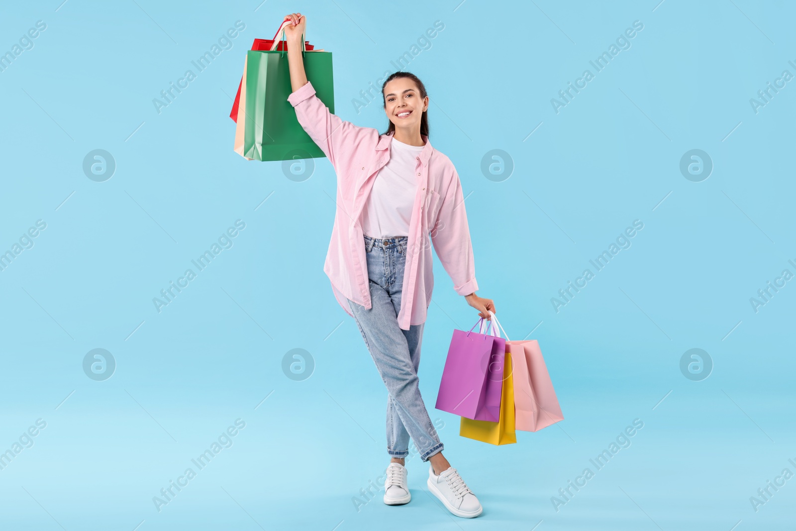 Photo of Smiling woman with colorful shopping bags on light blue background