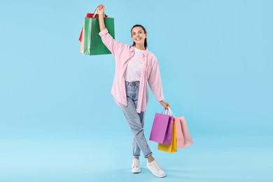 Photo of Smiling woman with colorful shopping bags on light blue background