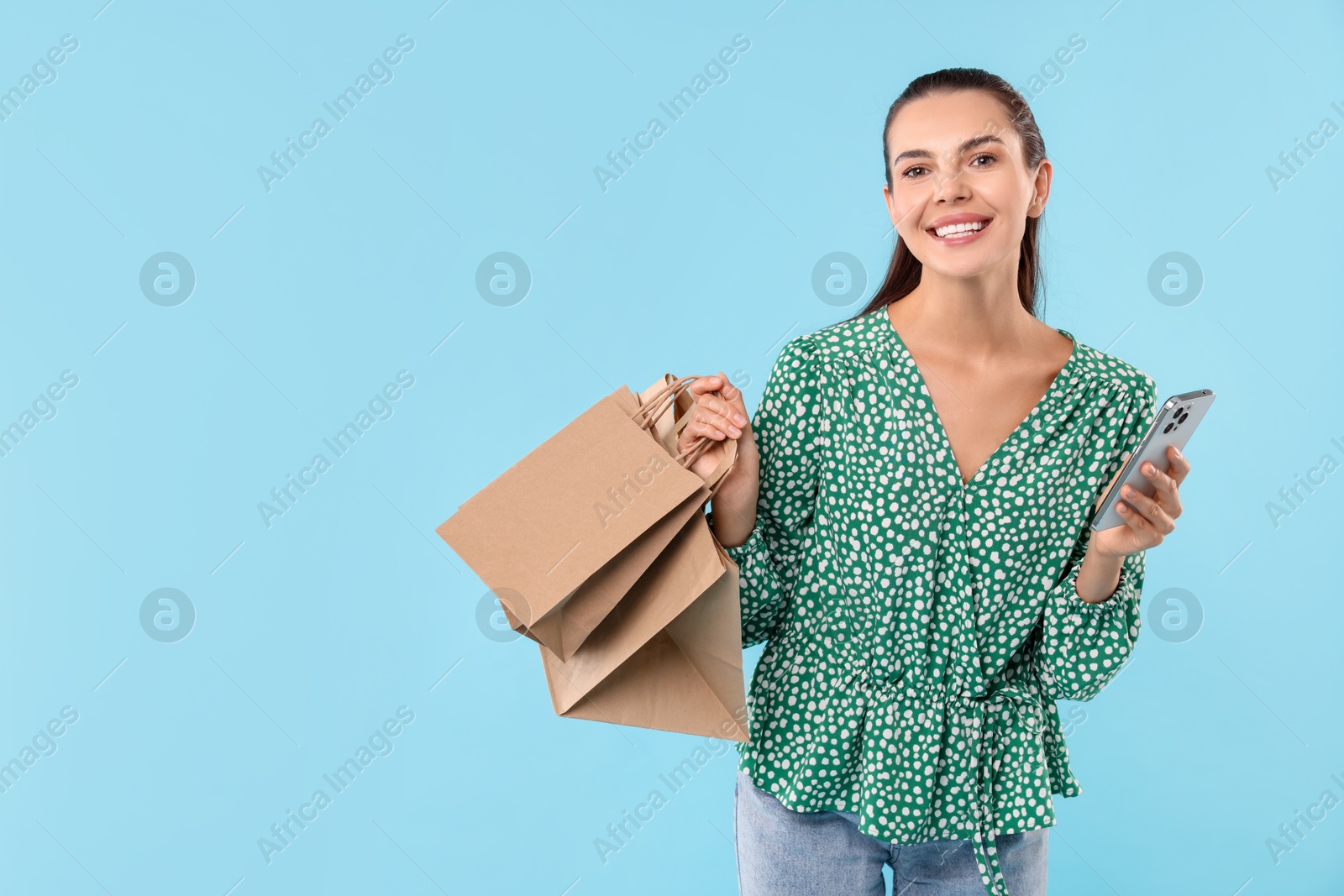 Photo of Smiling woman with shopping bags and smartphone on light blue background. Space for text