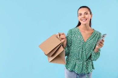 Smiling woman with shopping bags and smartphone on light blue background. Space for text