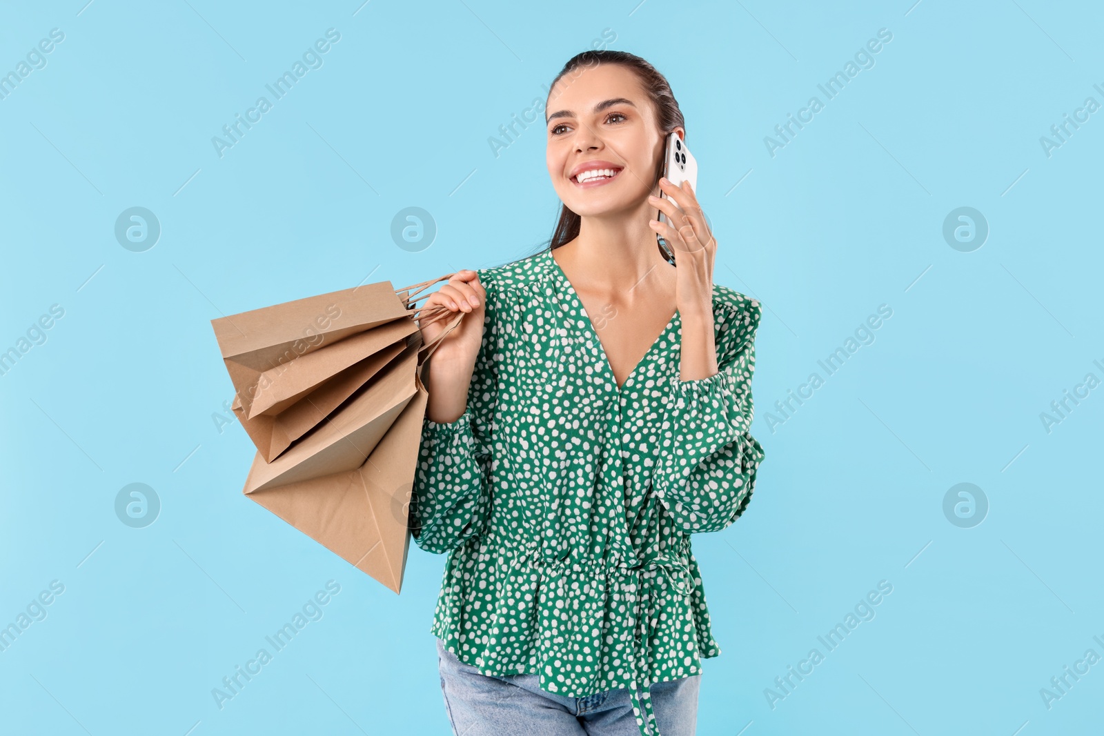 Photo of Smiling woman with shopping bags talking on smartphone against light blue background. Space for text