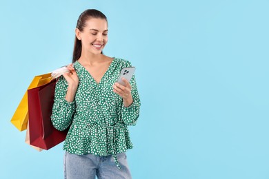 Photo of Smiling woman with shopping bags and smartphone on light blue background. Space for text