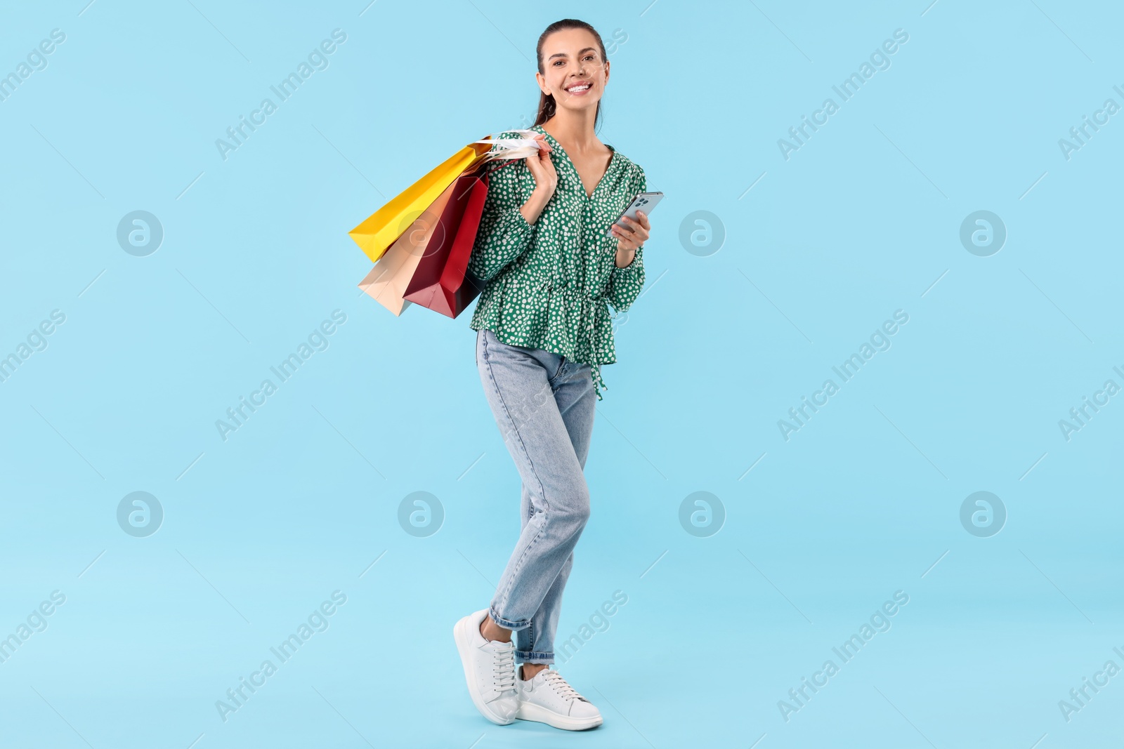 Photo of Smiling woman with shopping bags and smartphone on light blue background