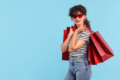 Beautiful woman with shopping bags on light blue background. Space for text