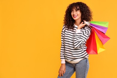 Smiling woman with colorful shopping bags on yellow background. Space for text