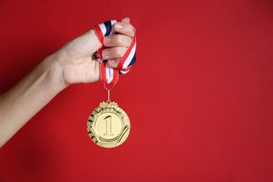 Photo of Woman with golden medal on red background, closeup. Space for text