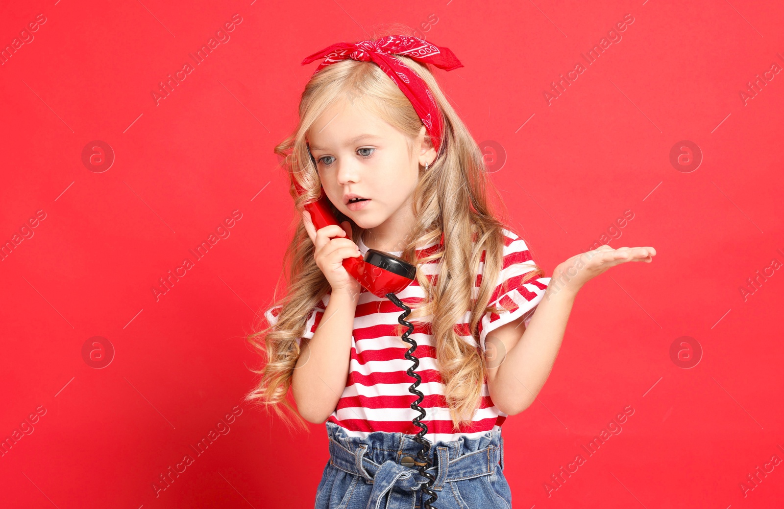 Photo of Cute little girl with handset of telephone on red background