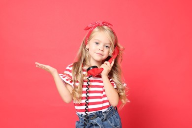 Cute little girl with handset of telephone on red background