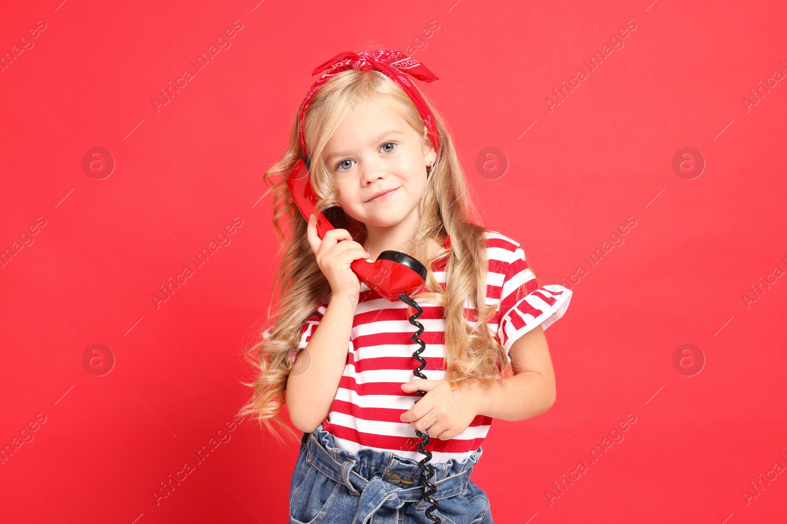 Photo of Cute little girl with handset of telephone on red background