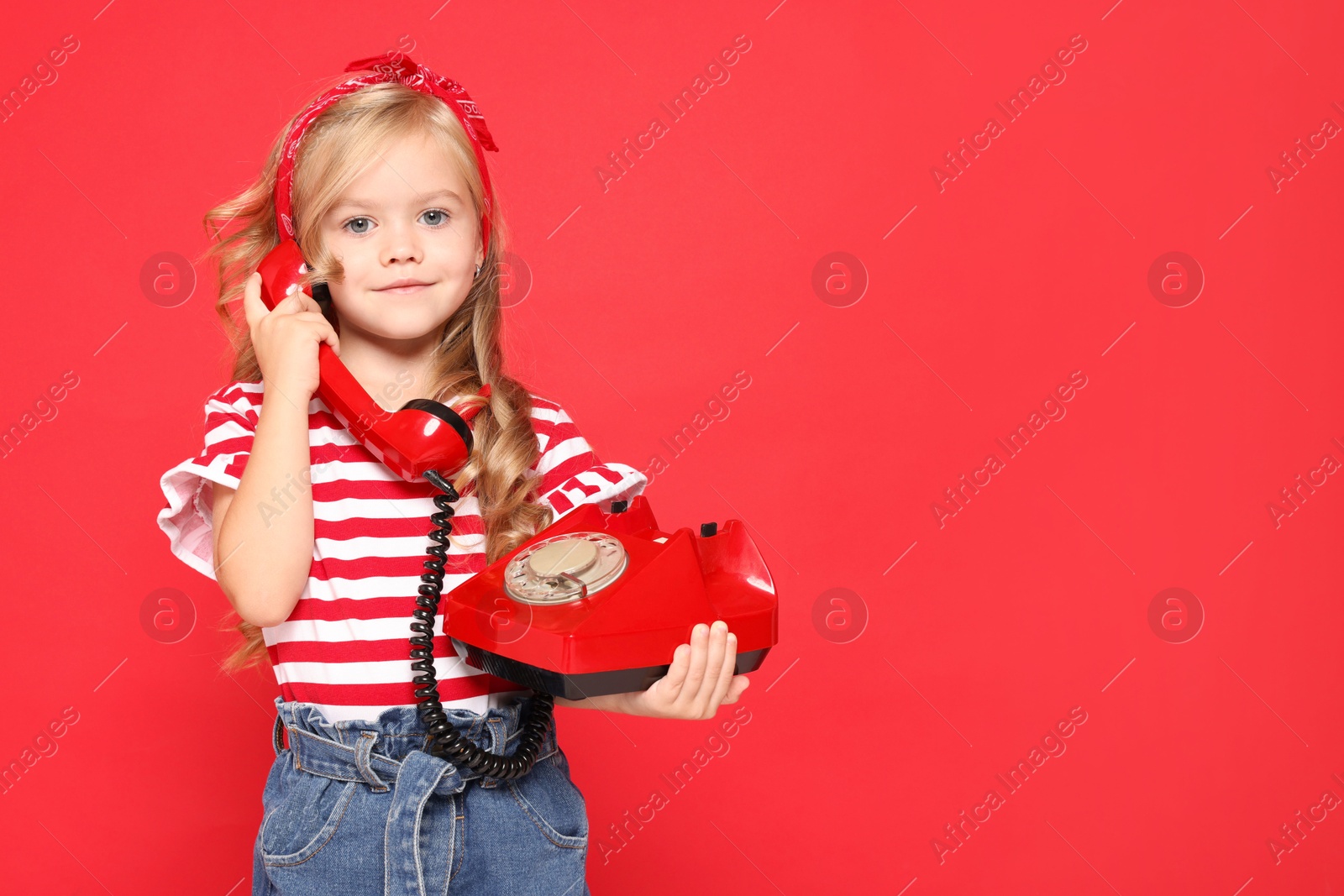 Photo of Cute little girl with telephone on red background, space for text