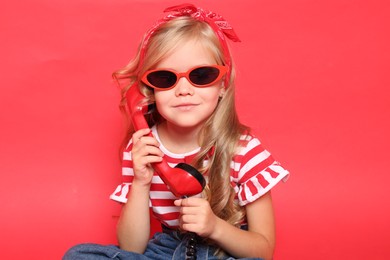 Cute little girl with handset of telephone on red background