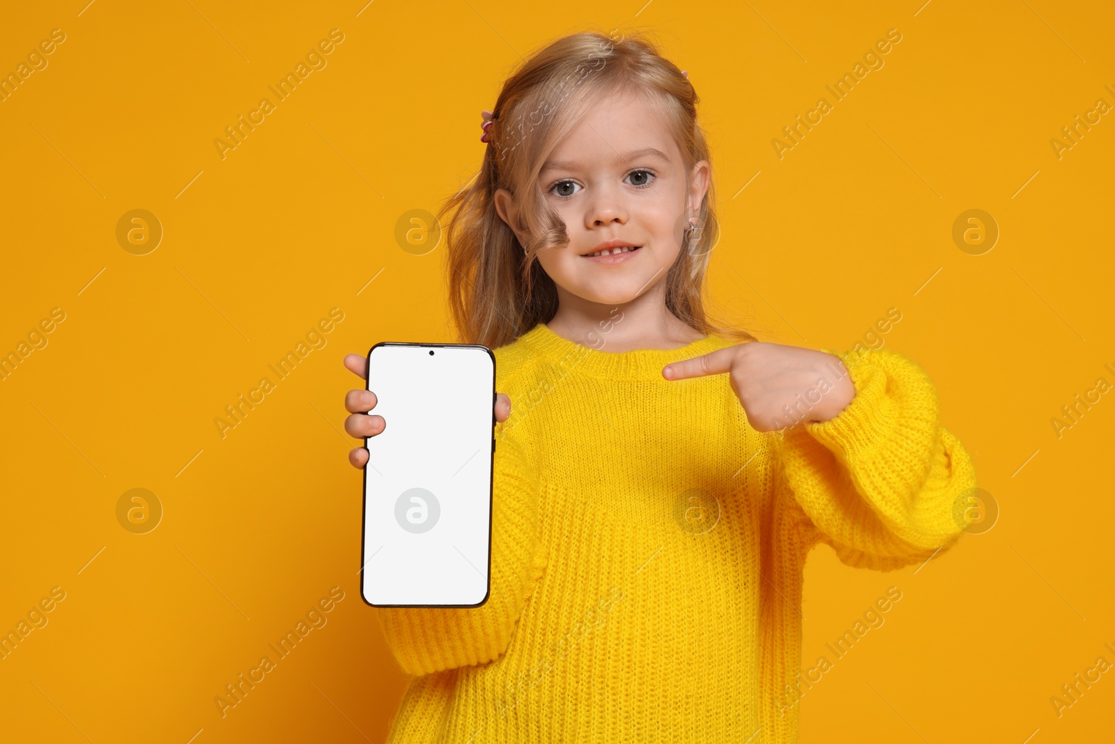 Photo of Cute little girl with smartphone against orange background