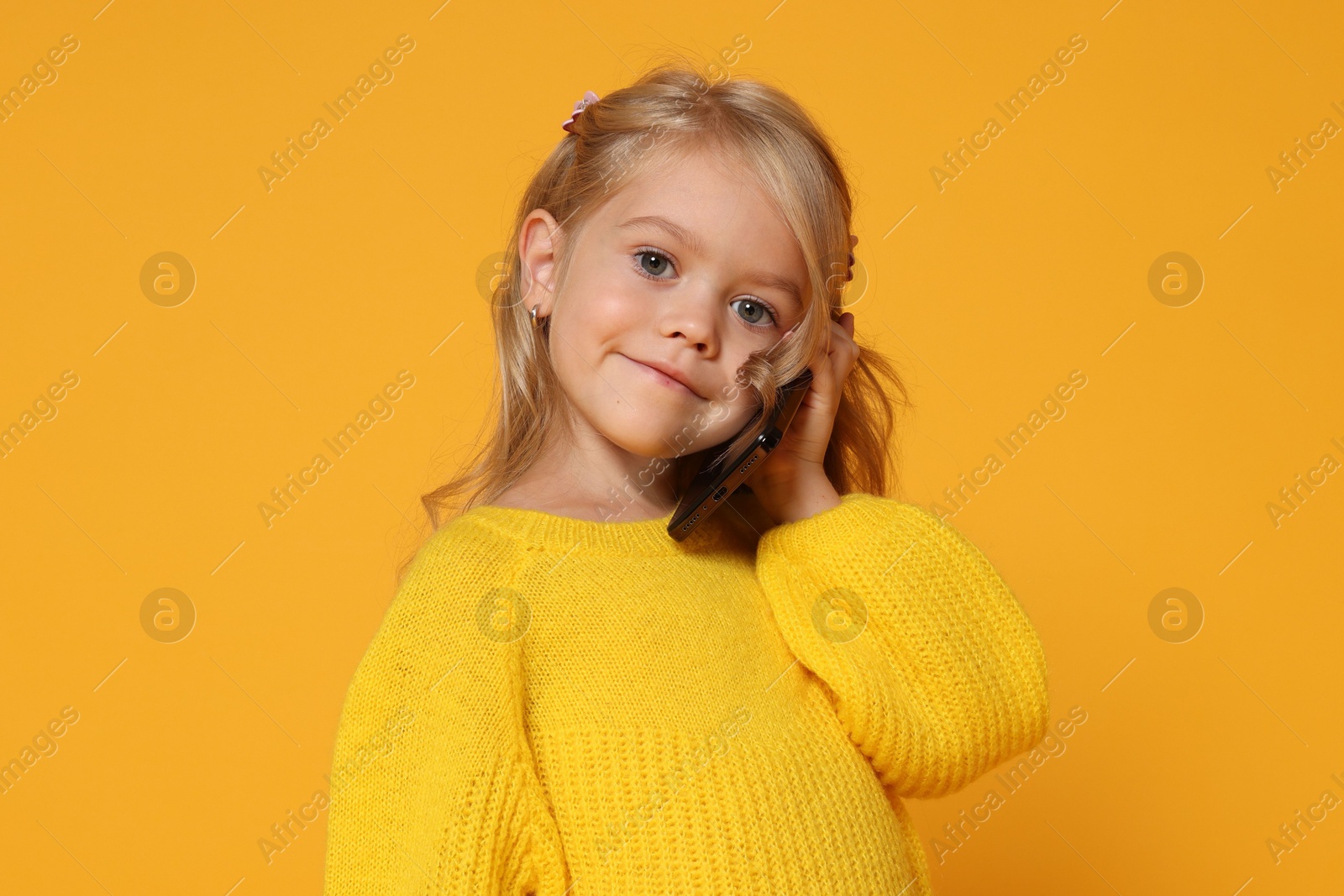 Photo of Cute little girl talking on smartphone against orange background