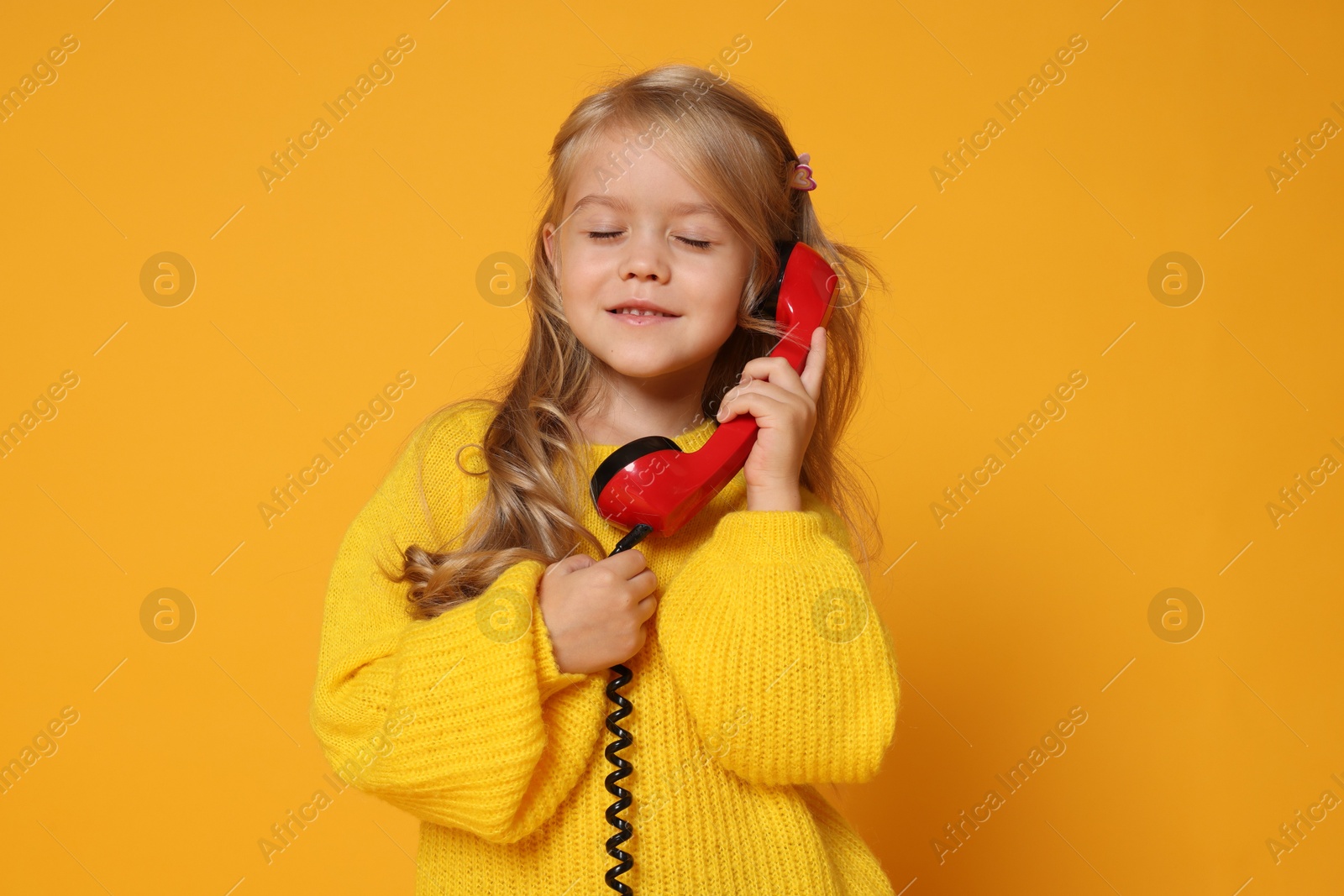 Photo of Cute little girl with handset of telephone on orange background