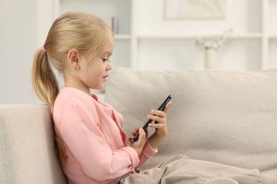 Cute little girl using smartphone on sofa at home