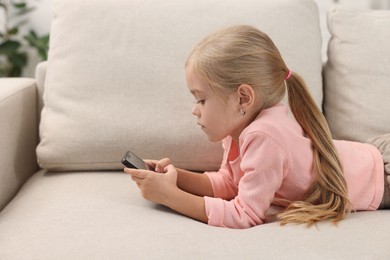 Photo of Cute little girl using smartphone on sofa at home