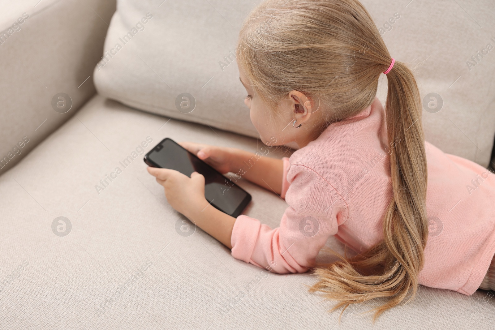 Photo of Cute little girl using smartphone on sofa at home