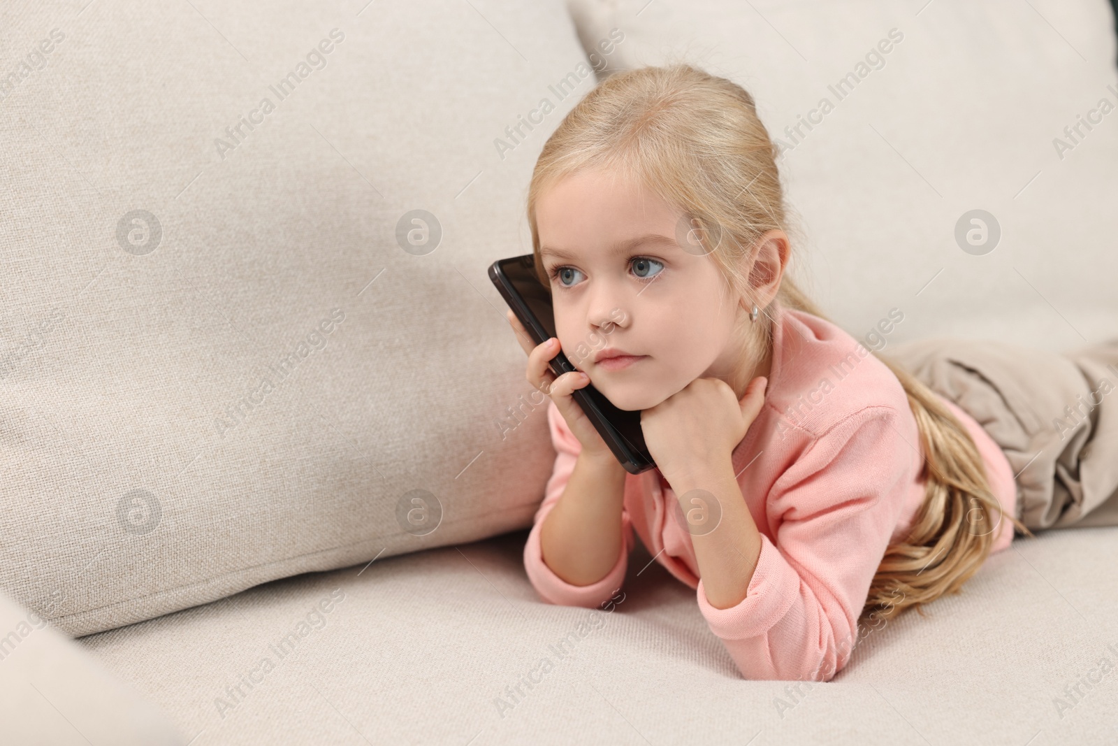 Photo of Cute little girl talking on smartphone at home, space for text